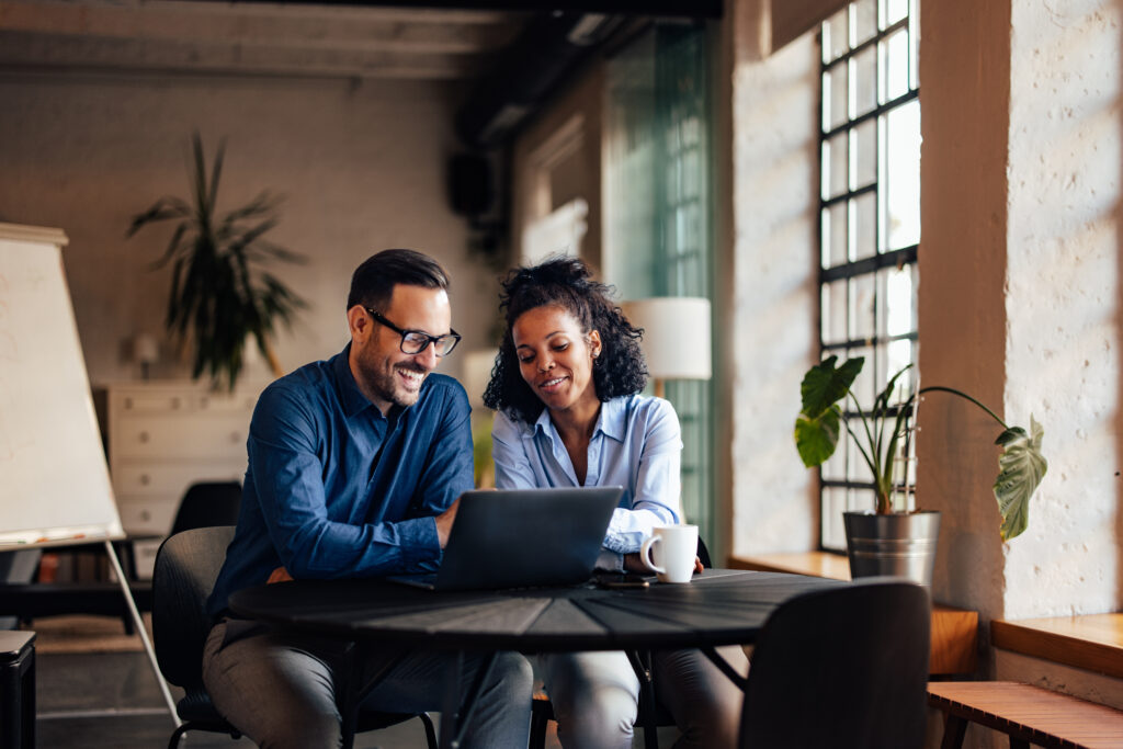 Two people sitting at a table looking at a laptop.